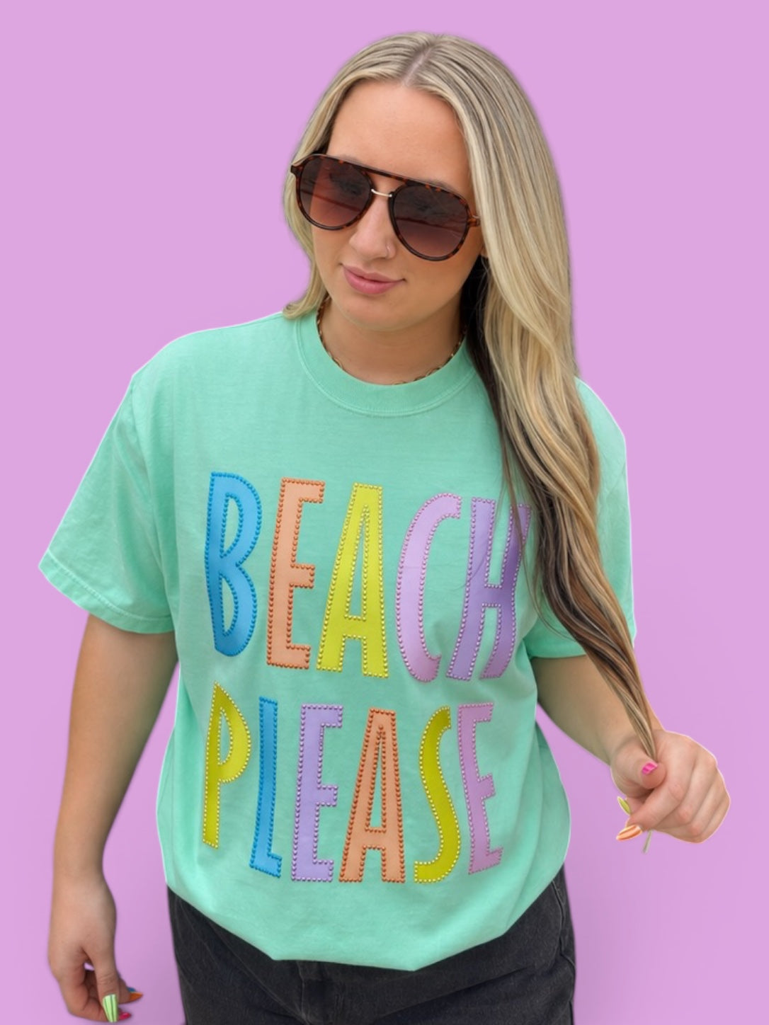 Woman wearing a green t-shirt with 'BEACH PLEASE' in colorful letters against a purple background