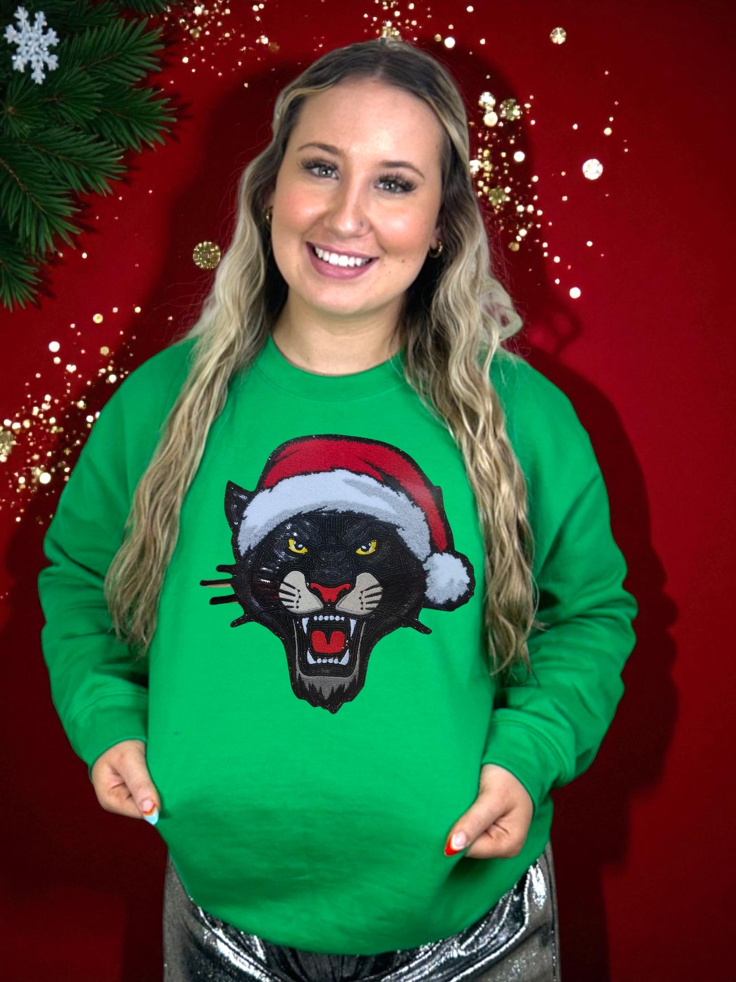 Woman wearing a green sweater with a panther sequin patch design in a Santa hat against a red background.