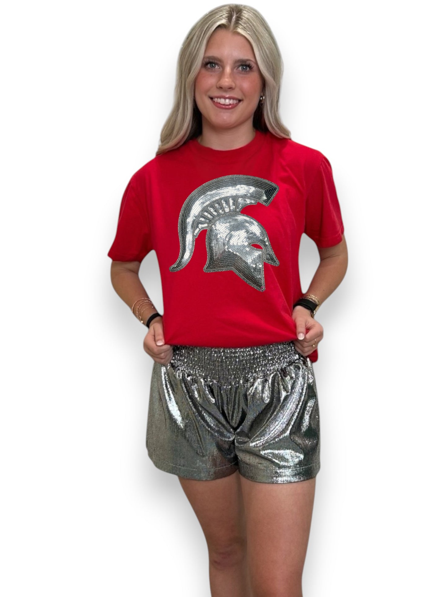 Woman wearing a red t-shirt with a silver logo and silver shorts on a white background