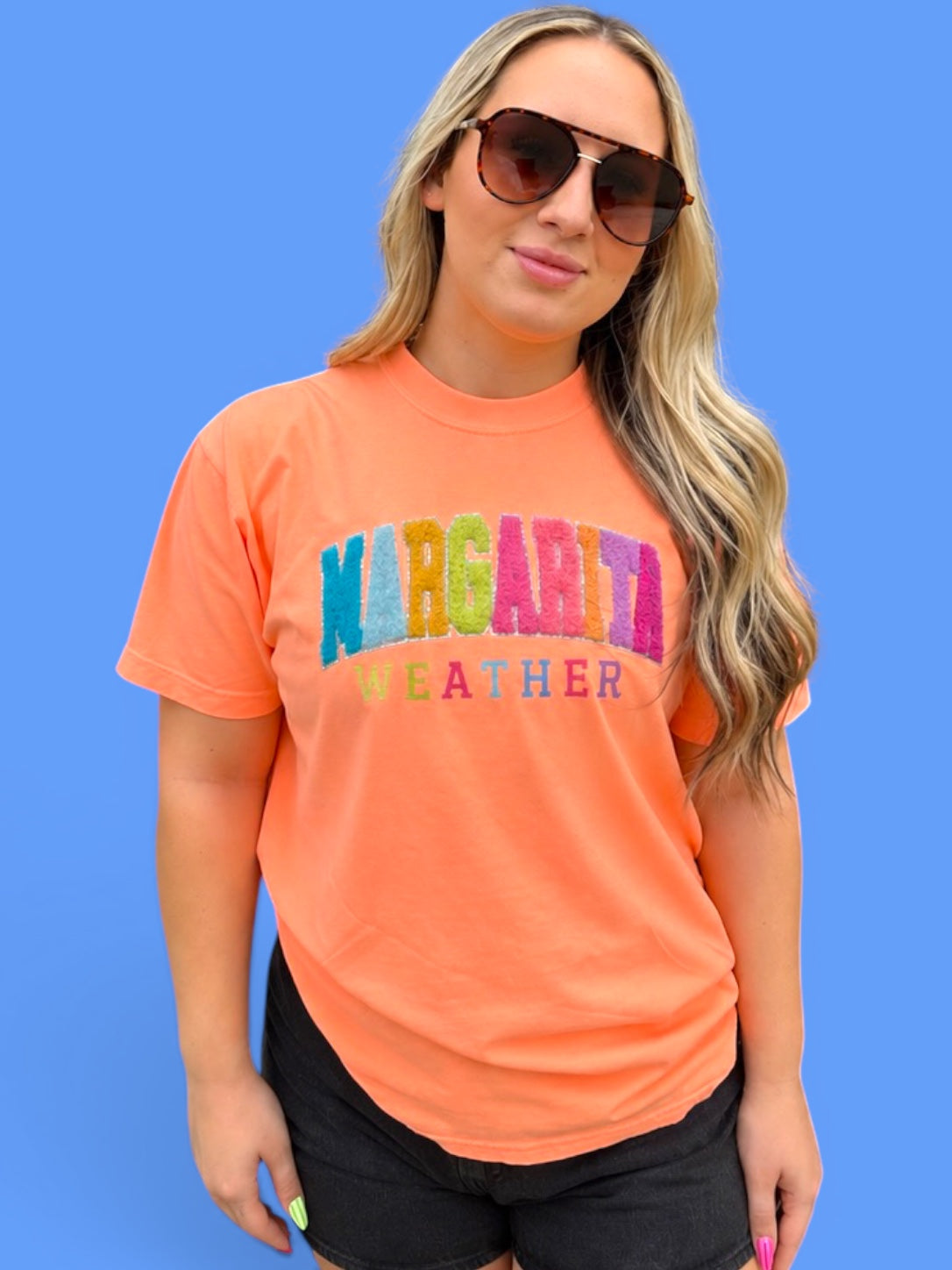 Person wearing an orange t-shirt with 'Margarita Weather' text on a blue background