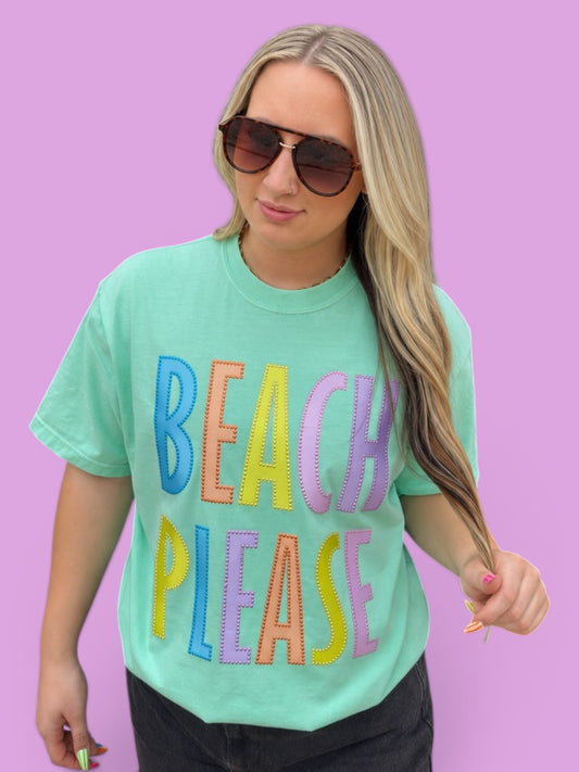 Woman wearing a green t-shirt with 'BEACH PLEASE' in colorful letters against a purple background