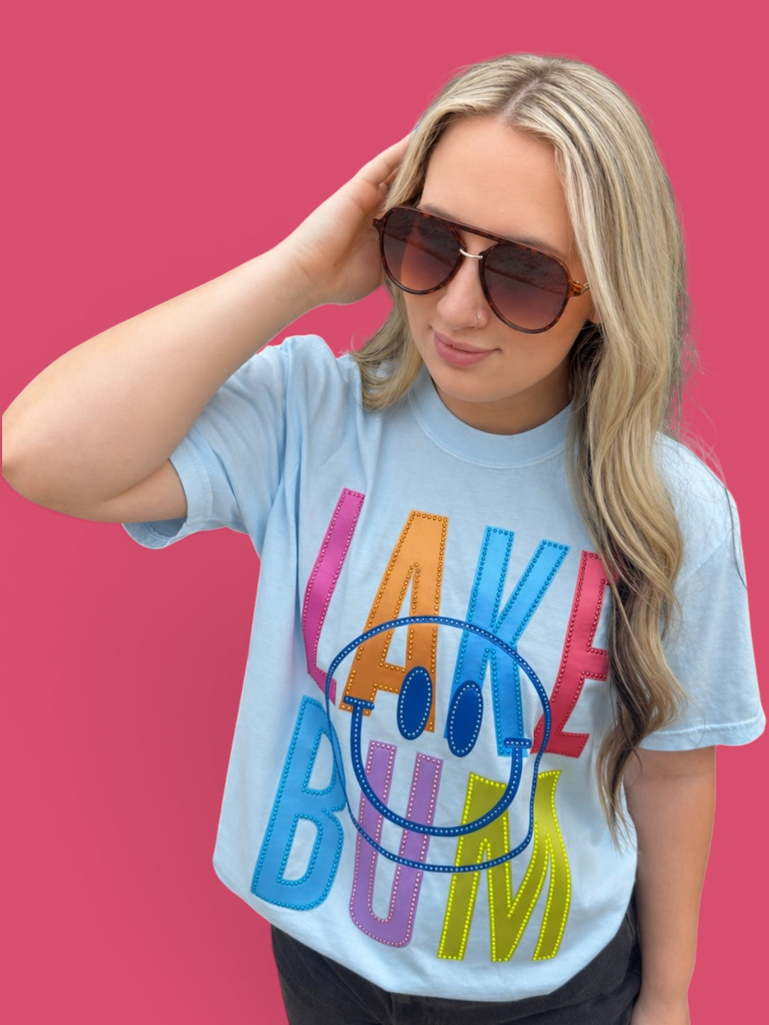 Woman wearing a colorful 'Lake Bum' t-shirt against a pink background