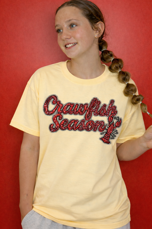 Person wearing a yellow t-shirt with 'Crawfish Season' text and lobster graphics against a red background