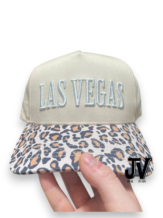 Cap with 'Las Vegas' text and leopard print visor held by a hand on a white background