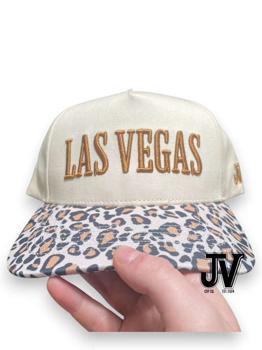 Cap with 'Las Vegas' text and leopard print brim held by a hand, with 'JV' logo in corner.