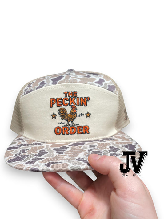 Trucker hat with 'The Peckin' Order' design held by a hand, on a white background.