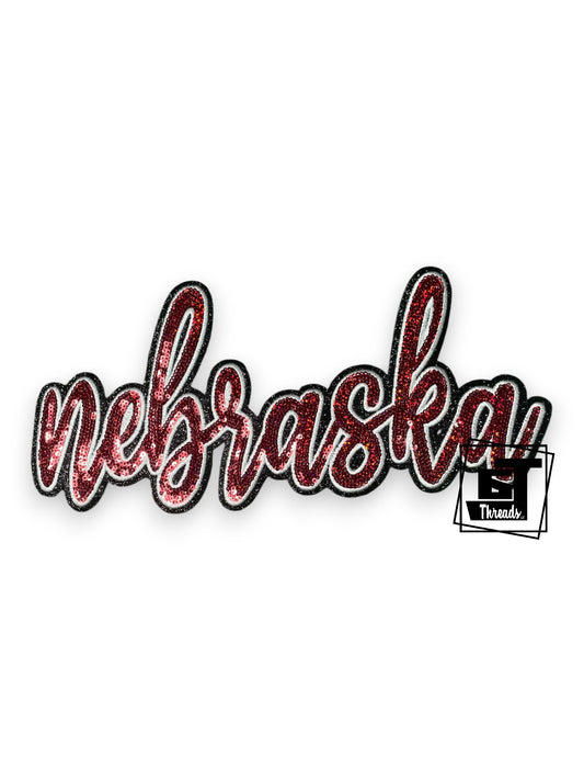Measurements: 11 inches wide by 5 inches tall
Red cursive sequin Nebraska with white embordiery and a black glitter background
Iron-on patch