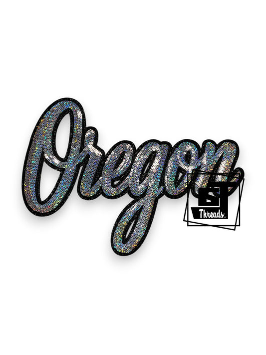 Measurements: 12 inches wide by 8 inches tall
Silver Cursive Sequin Oregon with black embroidery and black glitter background