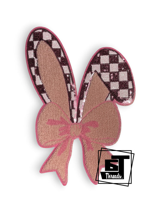 Measurements 7 inches wide by 11 inches tall
Sequin checkered and pink chenille bunny ears with bow with pink embroidery and pink glitter background
Iron-on Patch