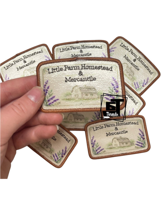 Hand holding a set of 'Little Farm Homestead & Mercantile' branded stickers with a white background.