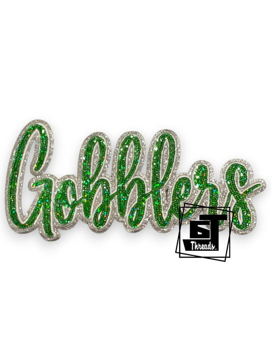 Green glittery 'Gobblers' text with a logo in the corner on a white background