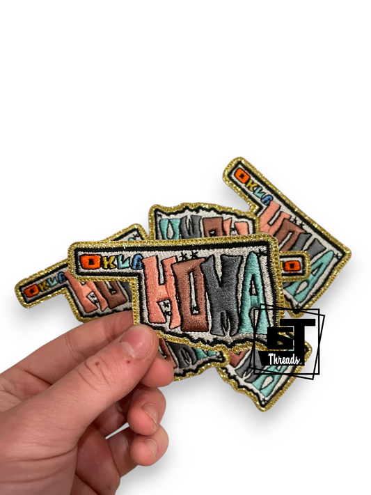 A hand holding three overlapping embroidered patches with a colorful retro-style design and gold glitter borders on a white background.
