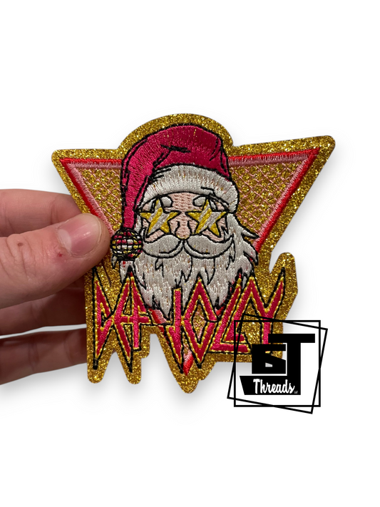 A hand holds an embroidered patch featuring a stylized Santa Claus with star-shaped eyes, a red hat, and a gold glitter outline, with the word 'PATRIOT' in red and black. A small 'BT Threads' logo watermark is visible in the lower right corner.
