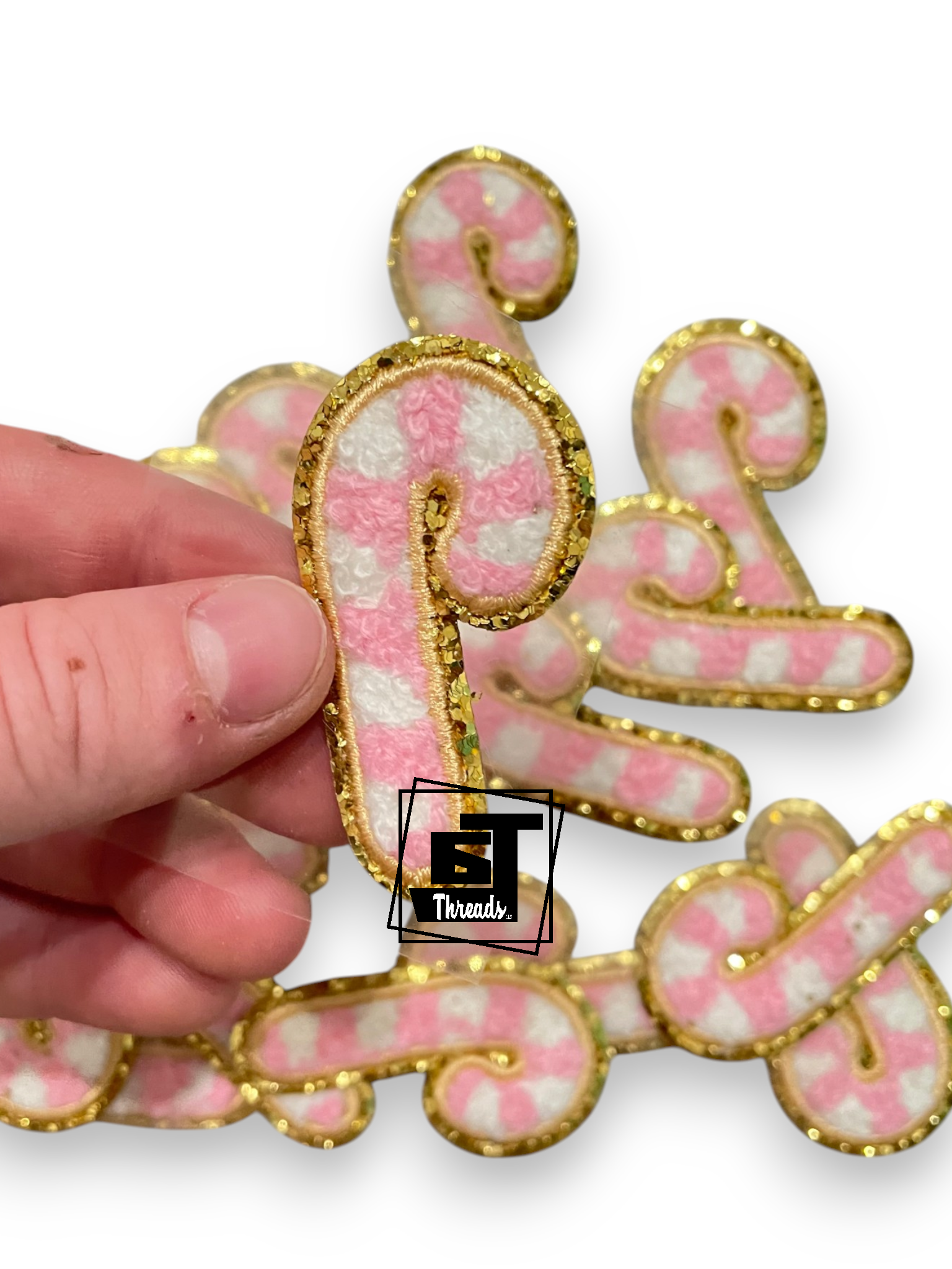 A hand holds a pink and white striped letter 'P' embellished with gold glitter trim, with other matching letters in the background on a white backdrop.
