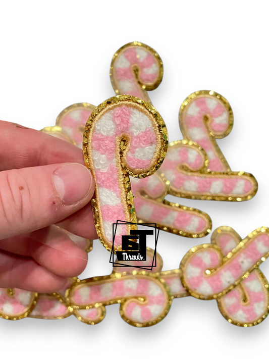 A hand holds a pink and white striped letter 'P' embellished with gold glitter trim, with other matching letters in the background on a white backdrop.