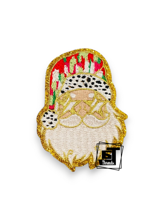 An embroidered patch of a Santa Claus face with a gold glitter outline, white beard, and a red hat with green and white patterns, shown on a white background with a small 'T Threads' logo sticker.