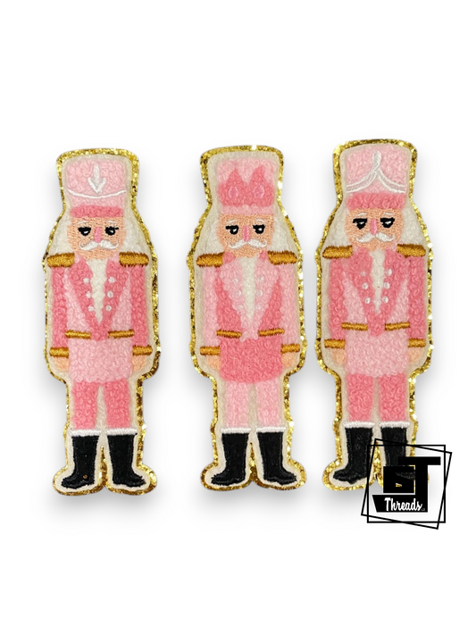 Three pink and gold nutcracker-shaped enamel pins with black boots, displayed on a clean white background.