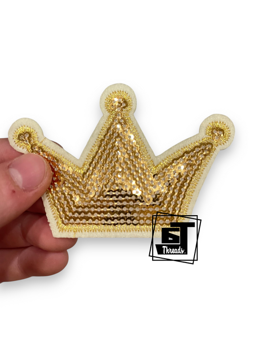 A hand holding a gold sequined crown-shaped patch with a white border, shown against a plain white background with a 'GT Threads' logo watermark.