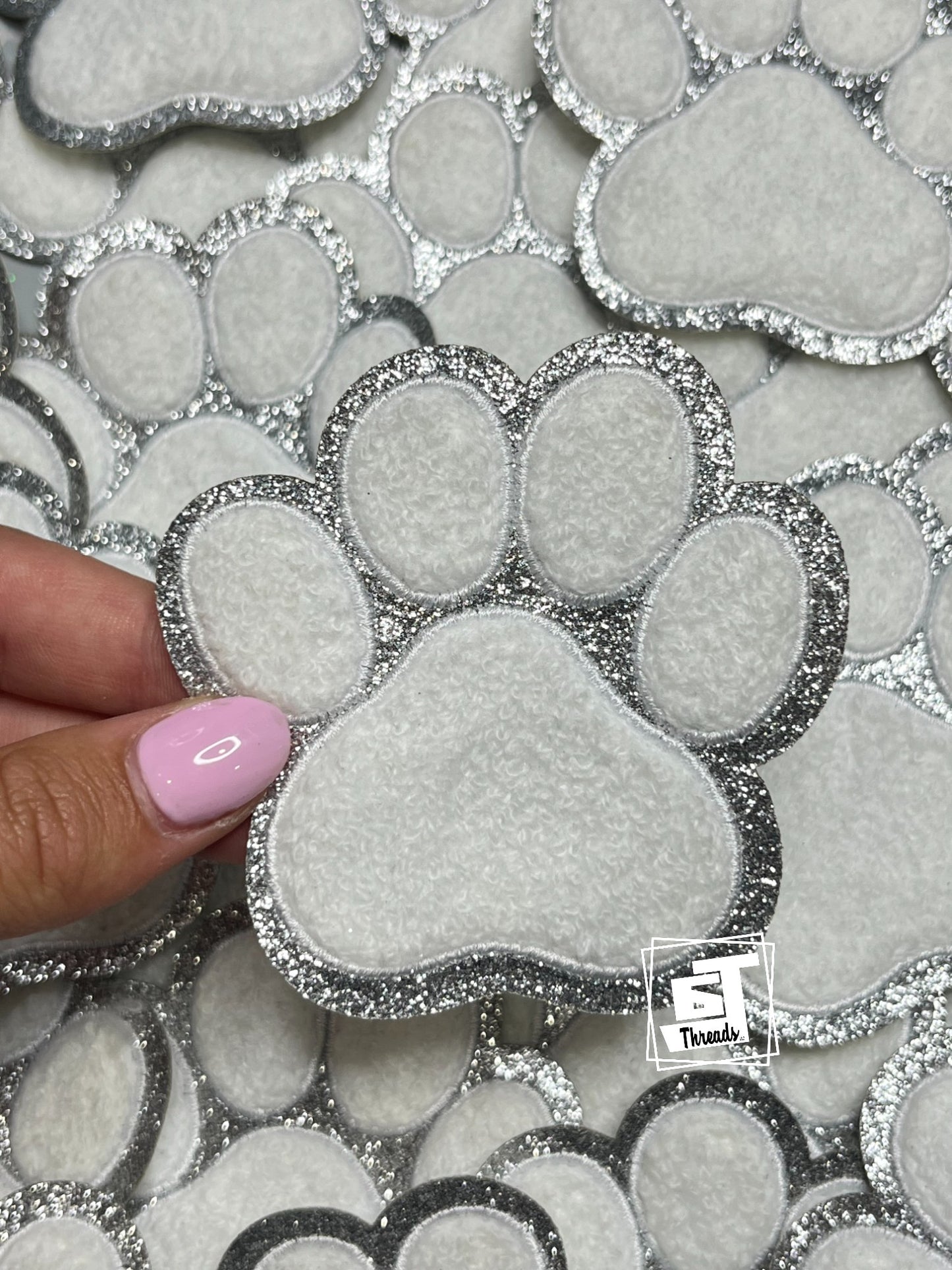 Silver glittery paw print design with a hand holding one of them, on a patterned background.