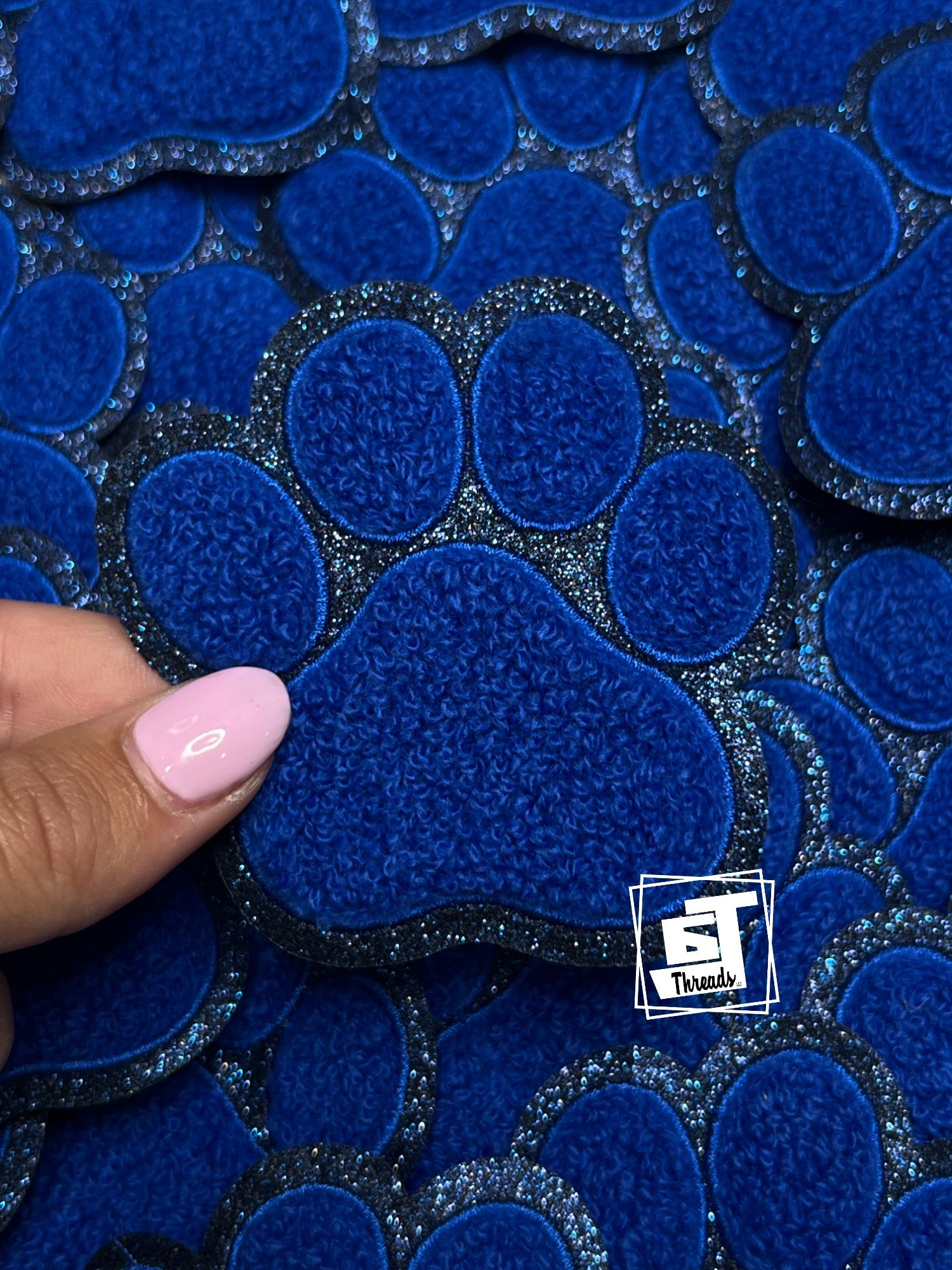 Blue textured material with a paw print design, held by a hand, branded 'ST Trends'.