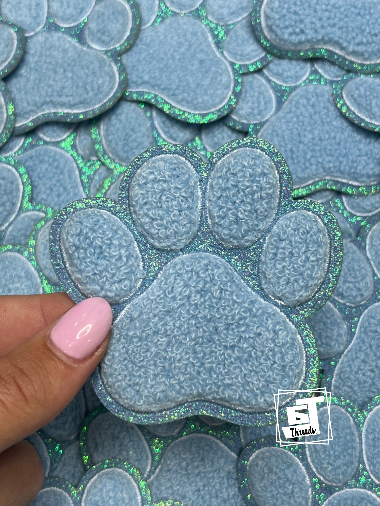 Heart-shaped blue patches with green glitter edges on a matching background, held by a hand.