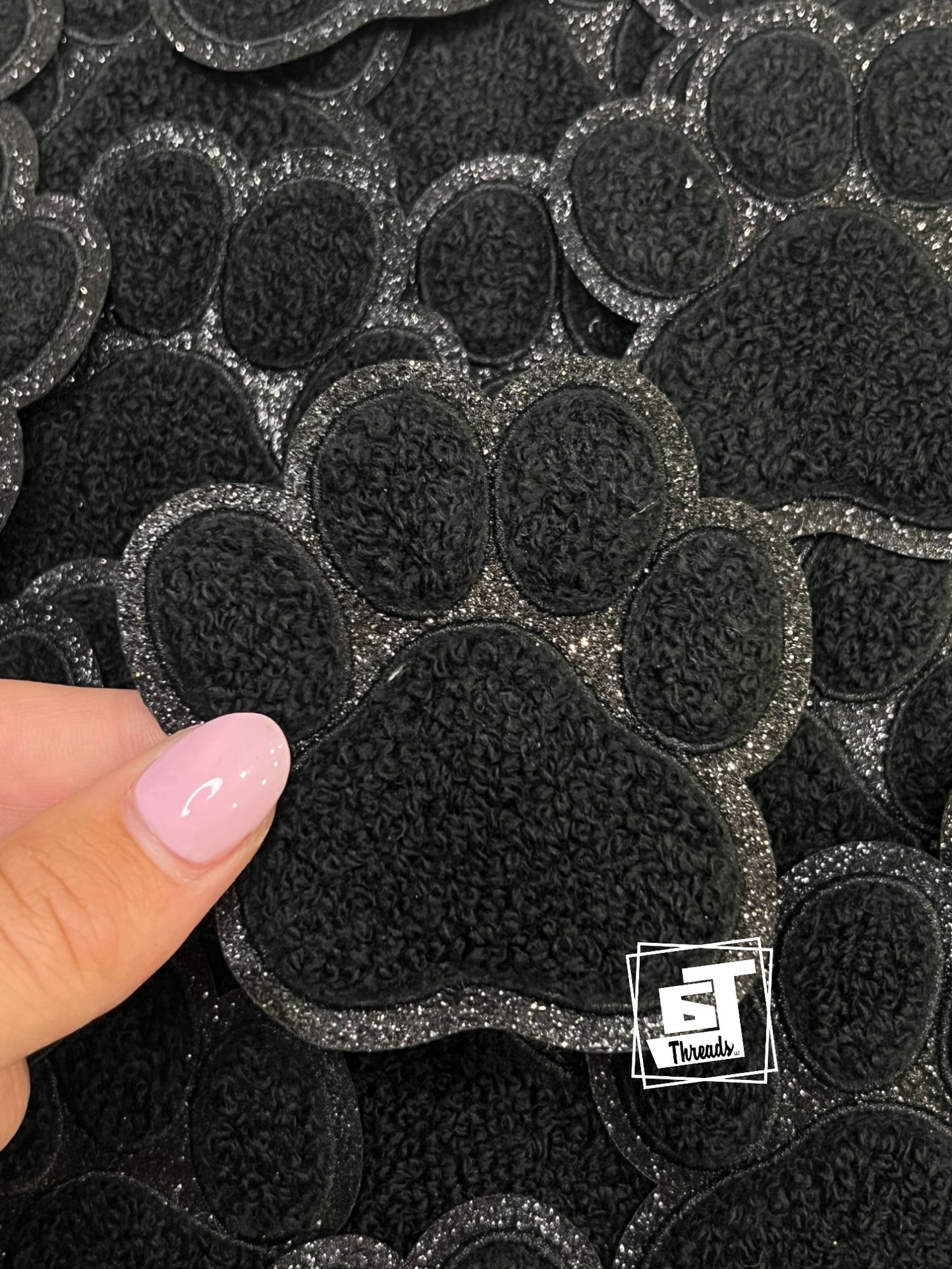 Black paw print patch held by a hand with a visible brand logo in the corner.