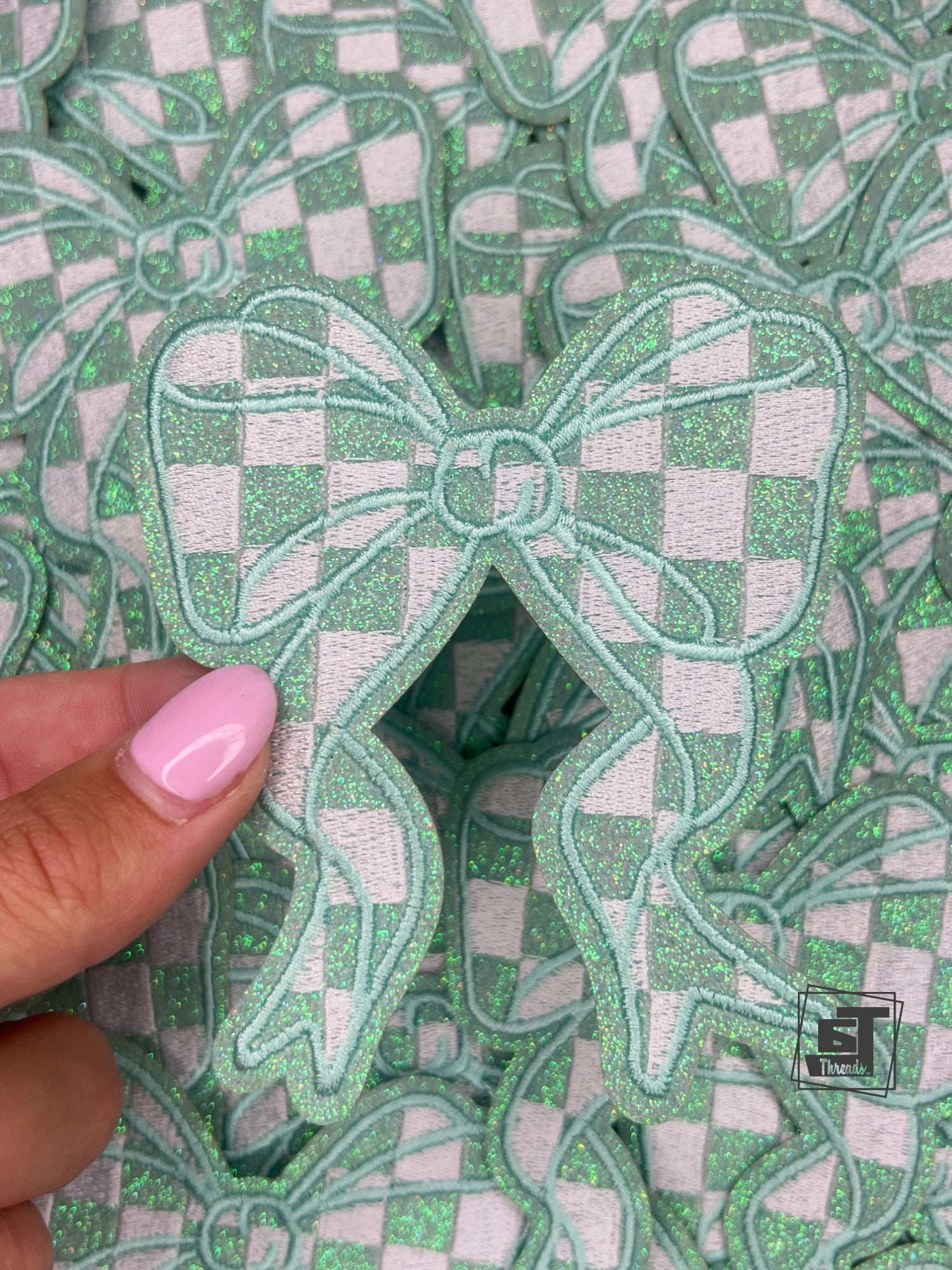Stack of green and white checkered bow-shaped patches with a hand holding one patch.