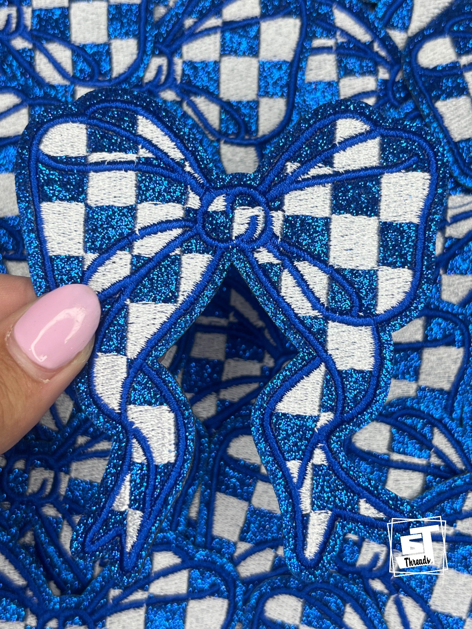 Close-up of blue embroidered fabric with a checkered pattern, held by a hand.