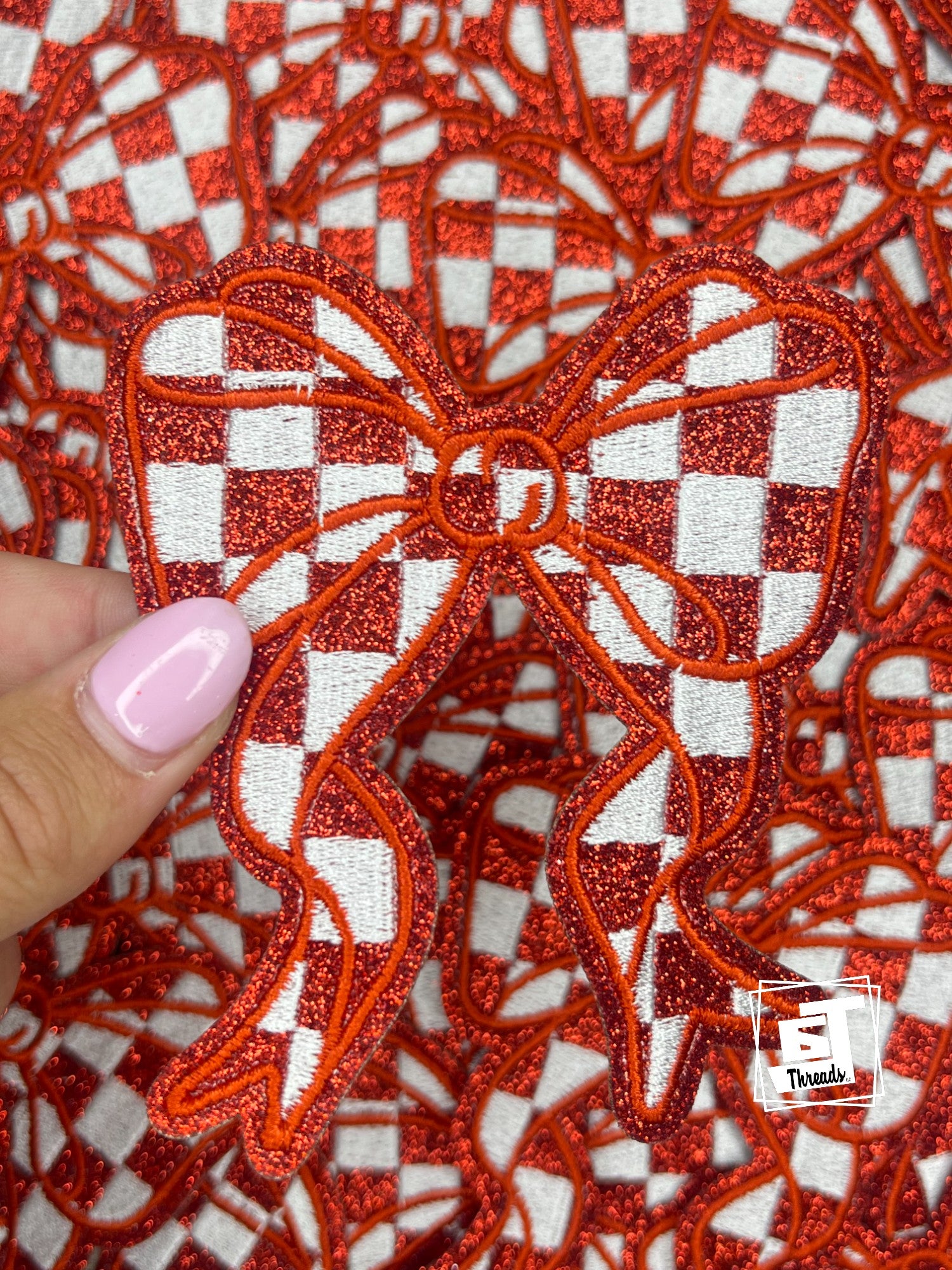 Red glittery bow patch held by a hand on a red and white checkered background