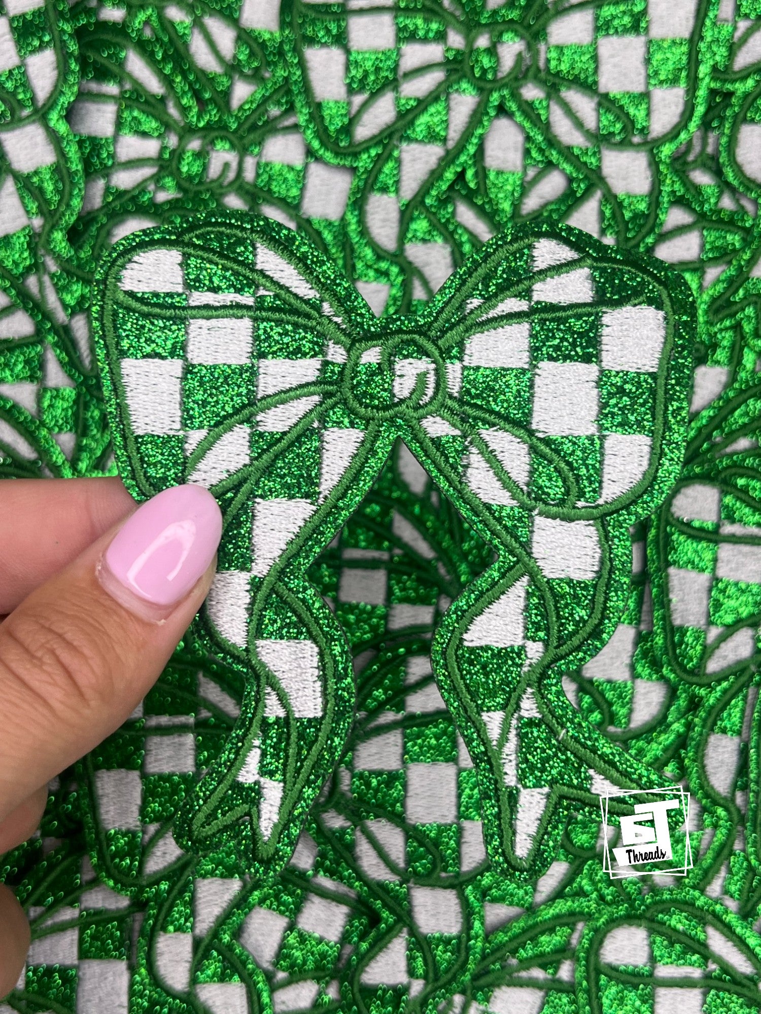 Close-up of green embroidered fabric with a checkered pattern, held by a hand.