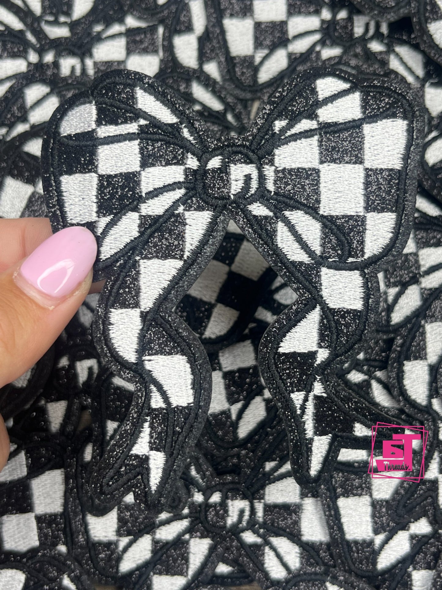 Black and white checkered bow design on fabric with a hand holding it.