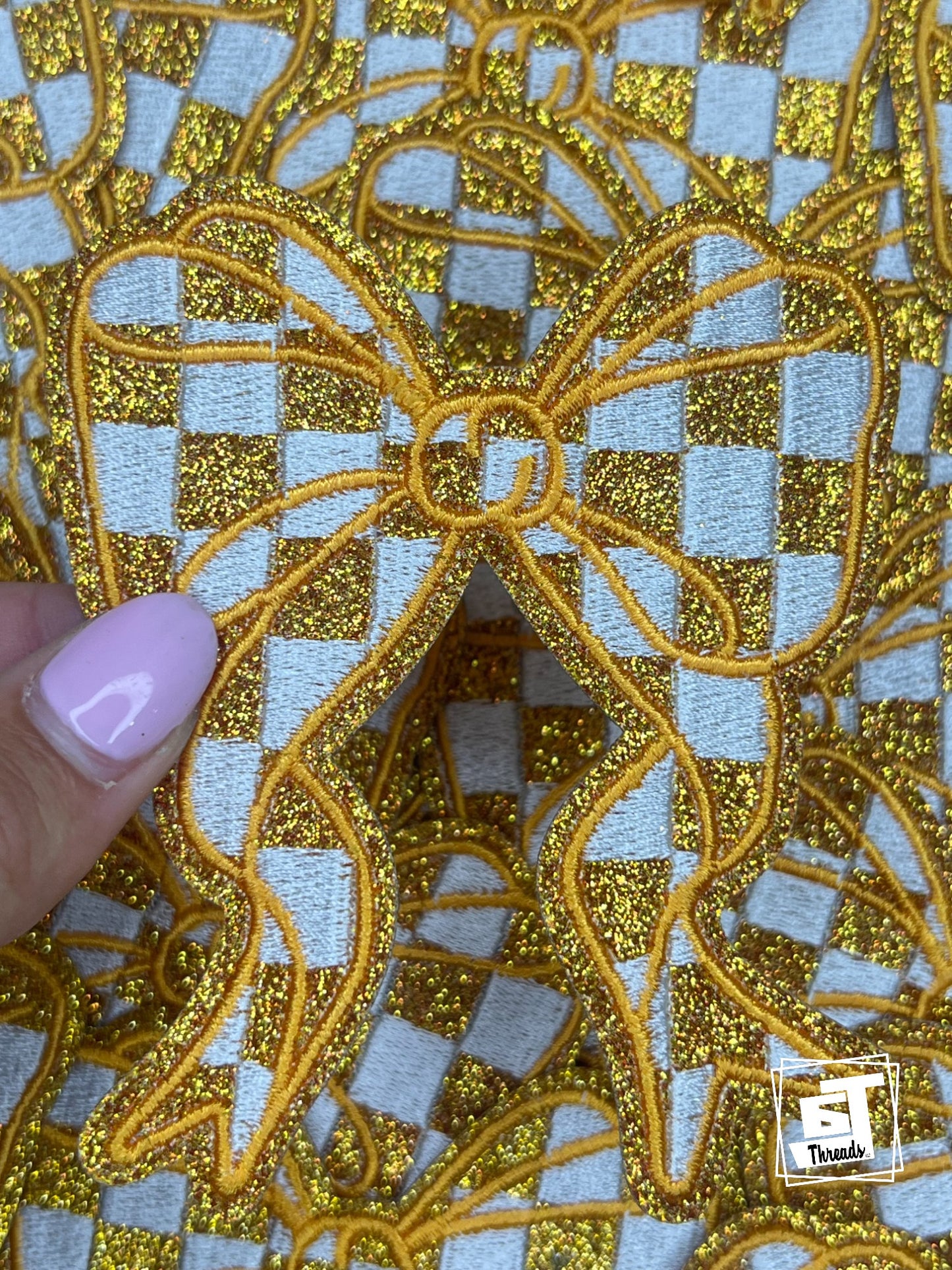 Gold embroidered fabric with a checkered pattern on a light blue background, held by a hand.