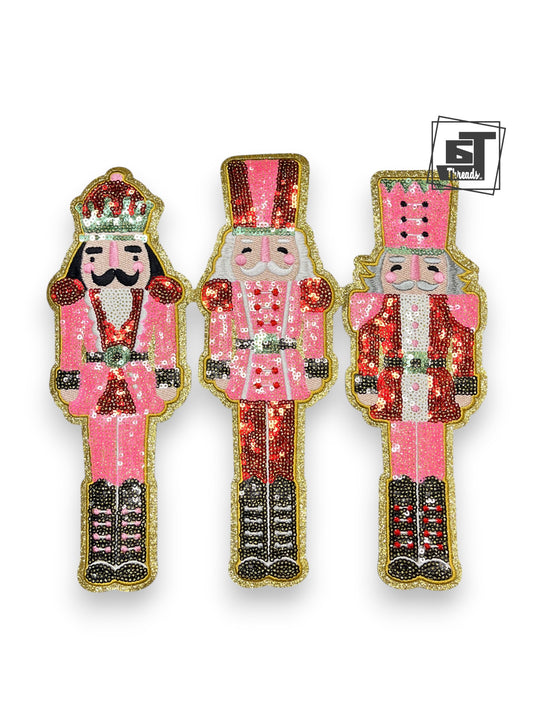 Three decorative nutcracker figures with pink and gold attire on a white background.