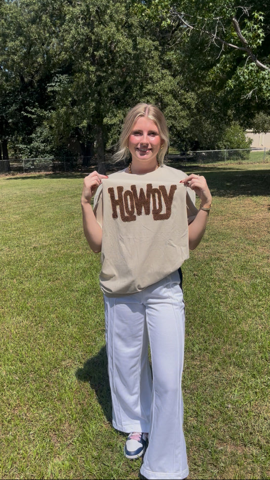 Person wearing a 'HOWDY' shirt outdoors on a grassy area with trees in the background