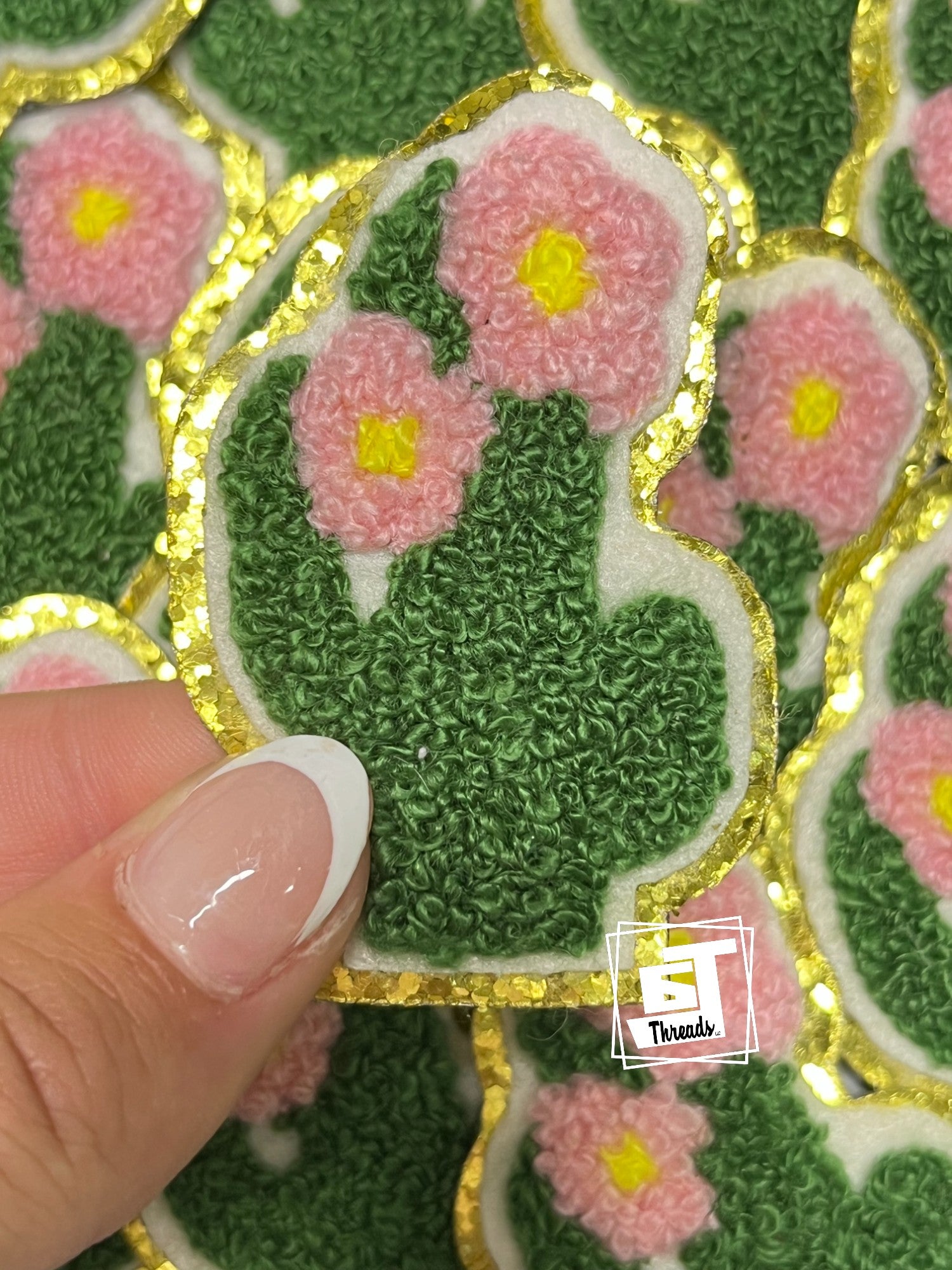 Decorative patch with pink flowers and green leaves held by a hand, brand 'ST Threads' visible.