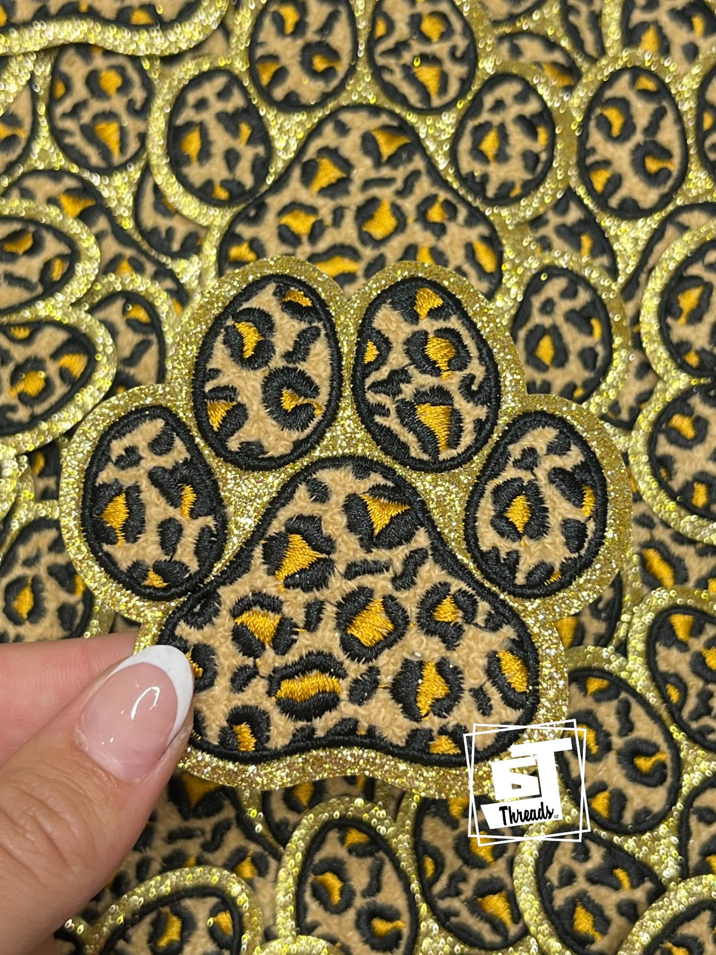 Leopard print paw patch on a gold glitter background with a hand for scale.
