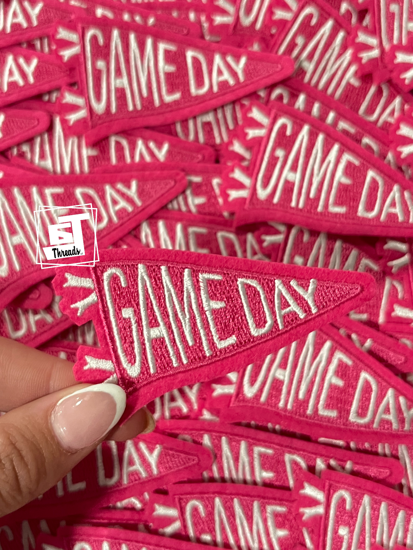 Pink 'GAME DAY' patches with a hand holding one above a pile.