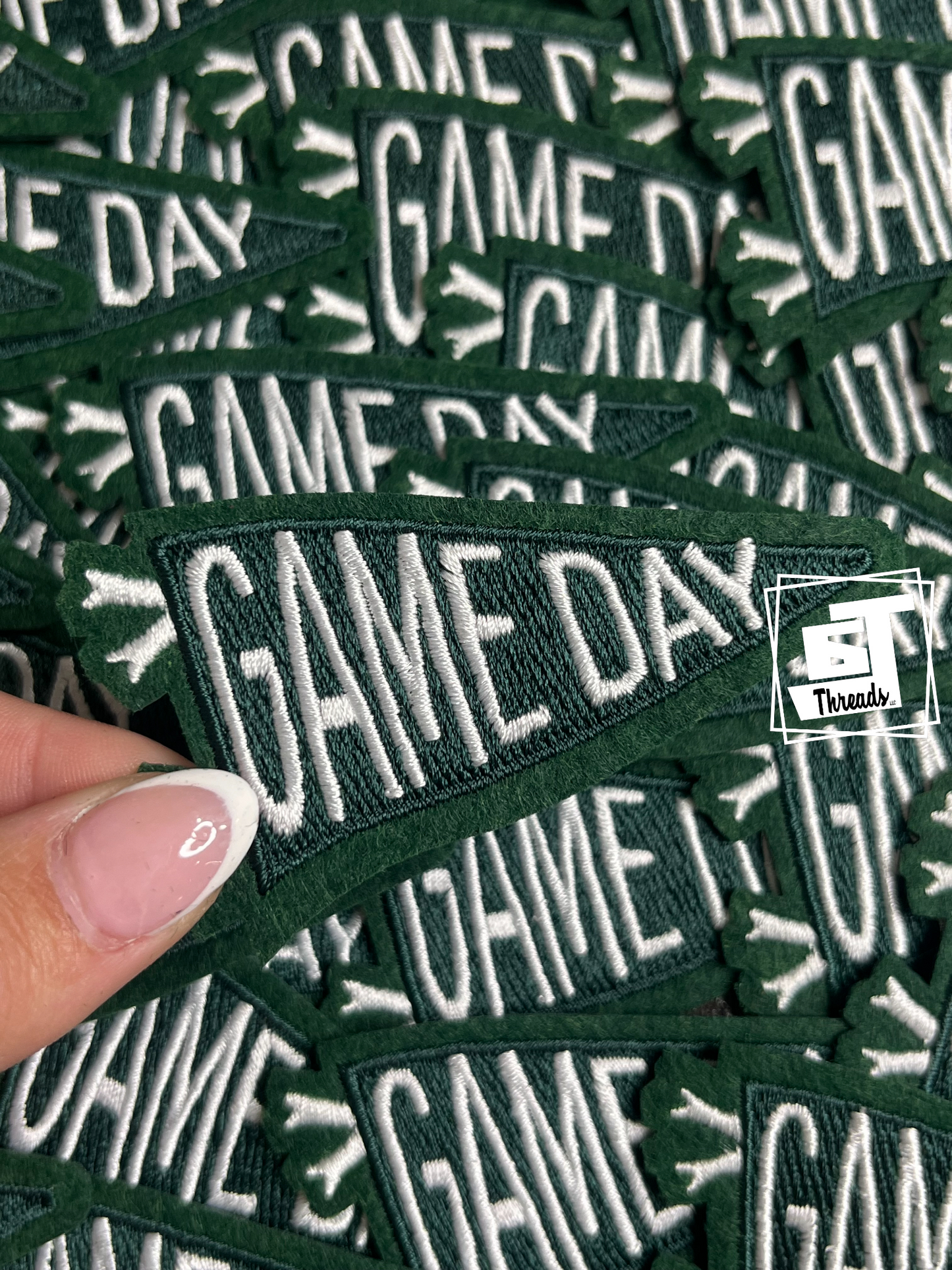 Stack of 'GAME DAY' patches with a hand holding one patch.