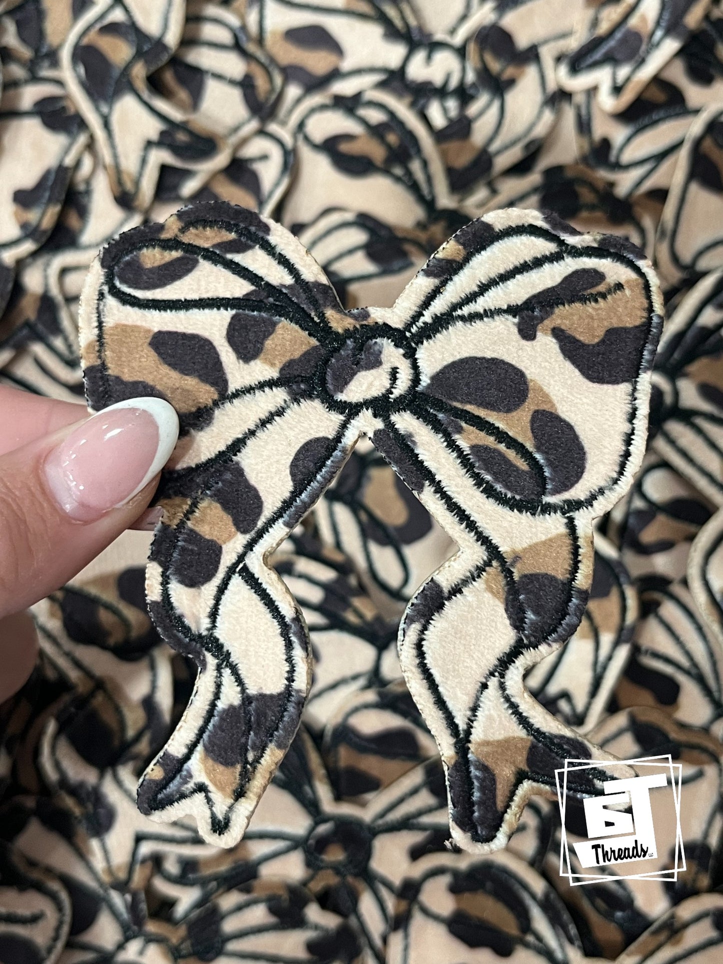 Leopard print bow-shaped patch held by a hand against a patterned background