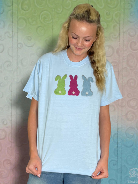 Person wearing a light blue t-shirt with colorful bunny designs against a patterned wall.
