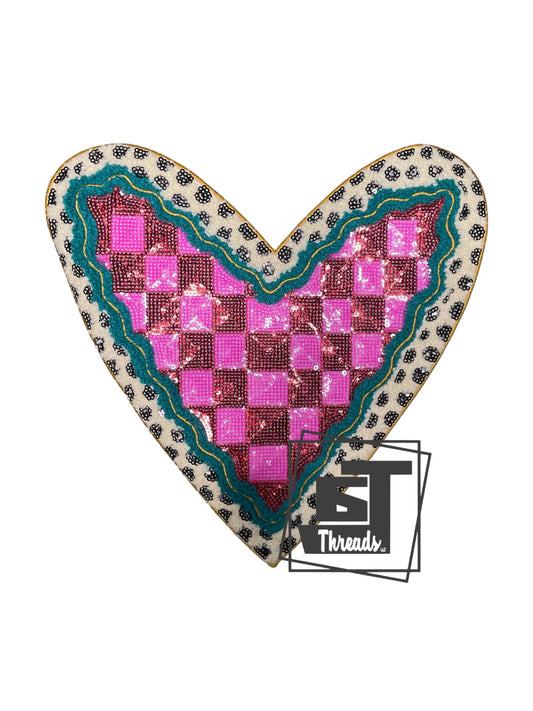 Featuring a striking 10" x 11" design, this iron-on patch showcases a pink and red checkered sequin heart accented with a teal curved border and delicate gold embroidery. The backdrop displays a luxe Chanel-inspired polka dot sequin pattern in complementary tones. Perfect for customizing apparel, bags, or accessories with eye-catching dimension and sparkle.
