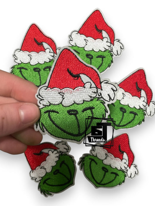 Set of Grinch face patches with Santa hats held by a hand on a white background.