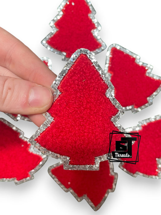 Red Christmas tree patches with a silver border held by a hand on a white background.