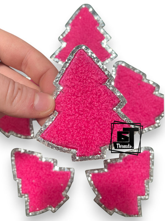 Pink tree-shaped fabric patches with silver borders on a white background, held by a hand.