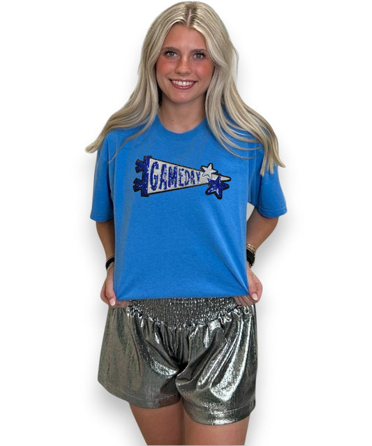 Woman wearing a blue t-shirt with 'Gameday' design and silver shorts on a white background