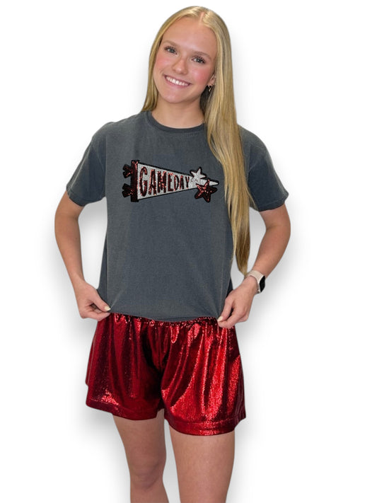 Person wearing a gray t-shirt with a 'GAMEDAY' logo and red shorts on a white background