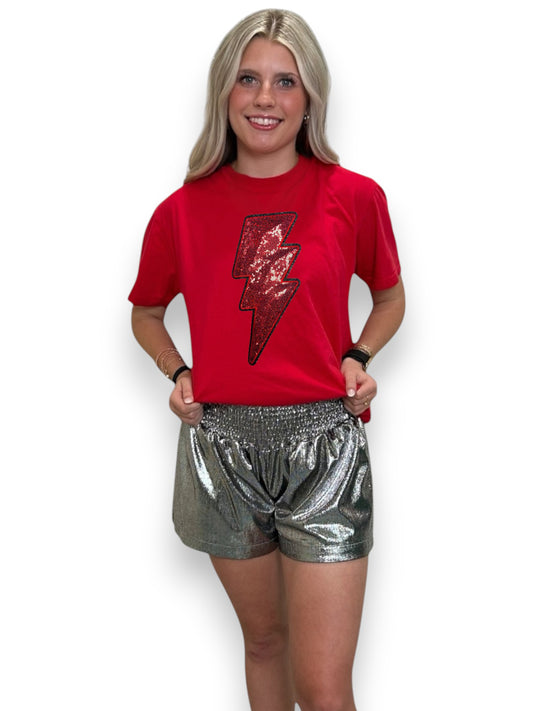 Woman wearing a red t-shirt with a sequin lightning bolt design and silver shorts on a white background