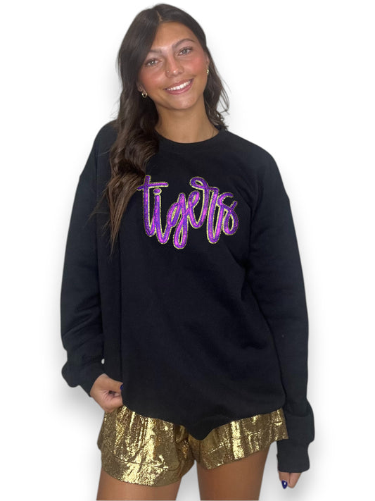 Person wearing a black sweatshirt with 'Tigers' in purple text and gold shorts on a white background