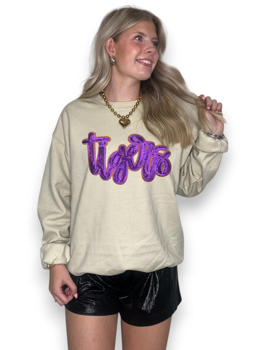 Woman wearing a beige sweatshirt with purple text and black shorts on a white background
