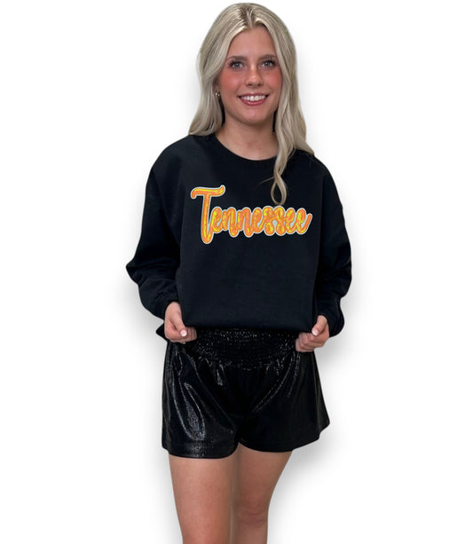 Woman wearing a black sweatshirt with 'Tennessee' in yellow text and black shorts on a white background